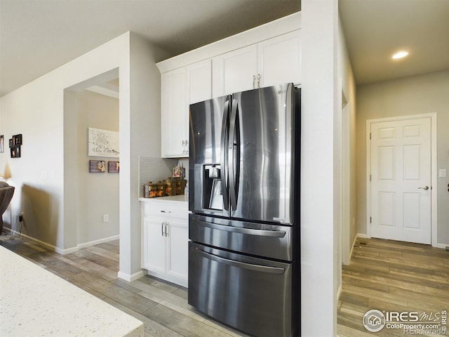 kitchen featuring wood finished floors, white cabinets, stainless steel fridge with ice dispenser, decorative backsplash, and light stone countertops