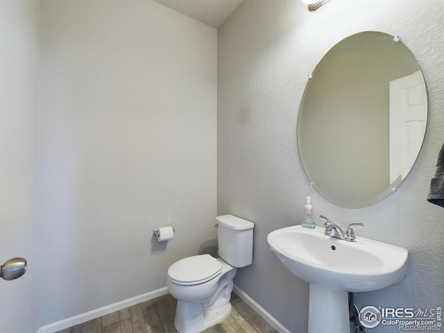 half bathroom with a sink, wood finished floors, toilet, and baseboards