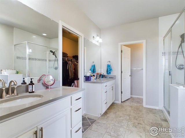 bathroom featuring a walk in closet, a shower stall, two vanities, and a sink