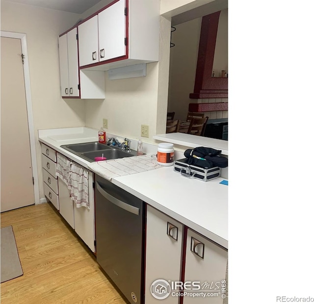 kitchen with light wood finished floors, white cabinets, dishwasher, light countertops, and a sink