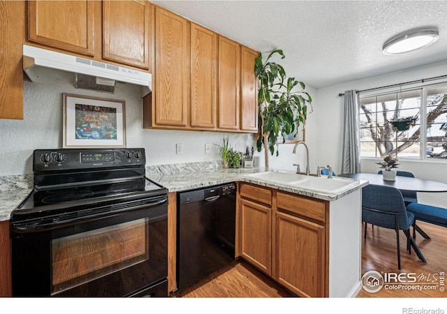 kitchen with under cabinet range hood, a peninsula, a sink, black appliances, and brown cabinetry