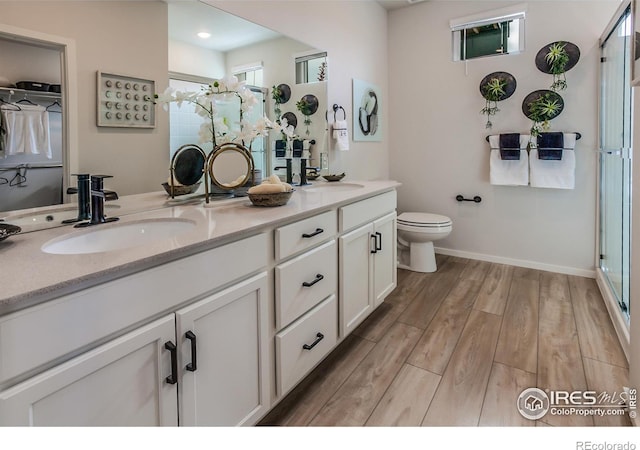 bathroom with a stall shower, double vanity, a sink, and wood finished floors