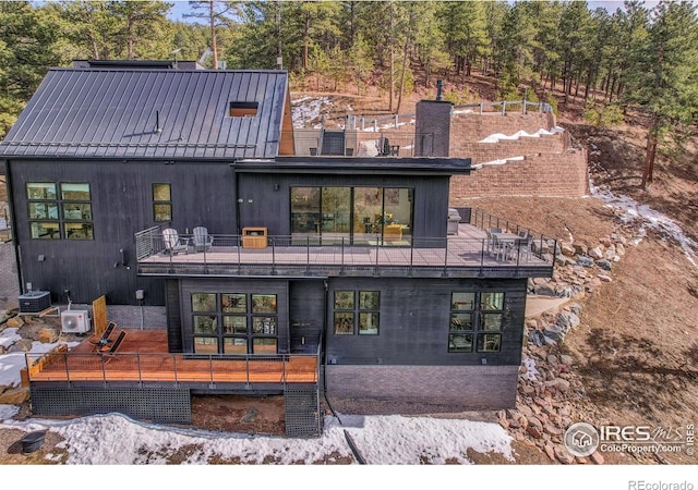 rear view of property featuring metal roof, central AC unit, and a balcony