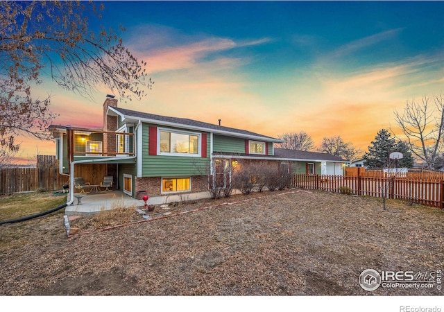 back of house with a balcony, a chimney, fence, a patio area, and brick siding