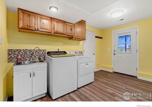 washroom with washer and clothes dryer, cabinet space, a sink, light wood-type flooring, and baseboards