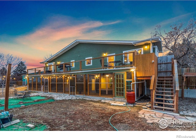 back of house at dusk featuring a patio area, stairway, and a balcony