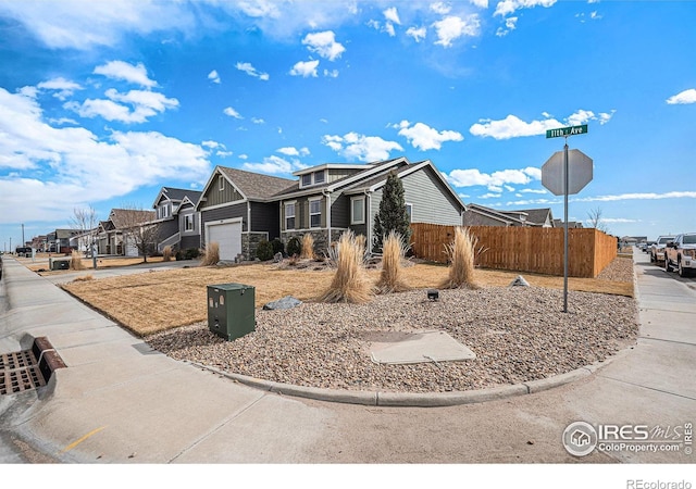 view of side of property featuring driveway, stone siding, a residential view, fence, and board and batten siding