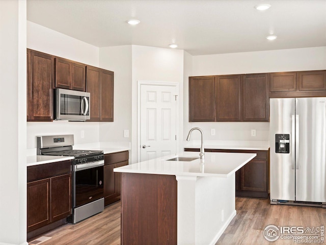 kitchen with light countertops, light wood-style flooring, appliances with stainless steel finishes, a sink, and dark brown cabinetry