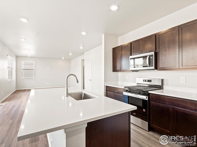 kitchen featuring stainless steel appliances, light countertops, a sink, and a center island with sink