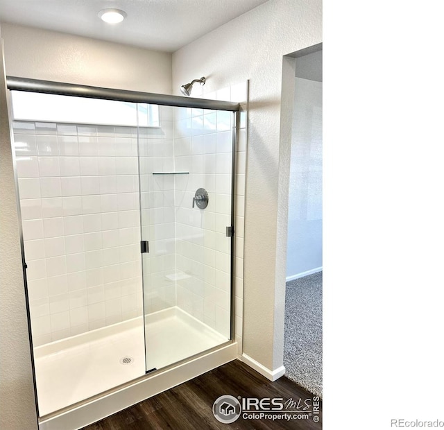 full bathroom featuring a textured wall, wood finished floors, a shower stall, and baseboards