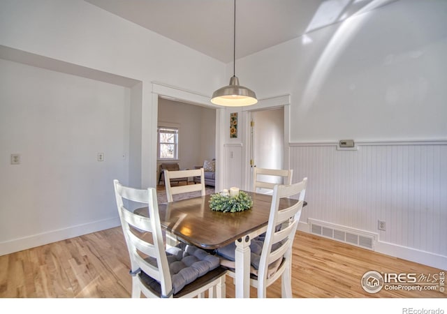 dining room with light wood-type flooring, a wainscoted wall, and visible vents