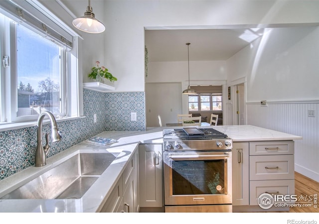 kitchen with a wainscoted wall, a peninsula, stainless steel gas range, light stone countertops, and a sink