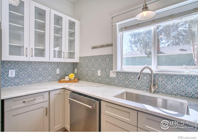 kitchen with a sink, stainless steel dishwasher, backsplash, light stone countertops, and glass insert cabinets