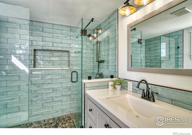 full bathroom with visible vents, a shower stall, vanity, and a textured ceiling