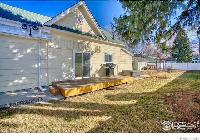 rear view of house featuring a shingled roof, an outbuilding, fence, a deck, and a yard