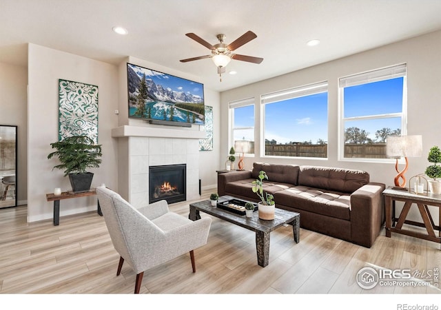 living room with baseboards, a tiled fireplace, light wood-style flooring, and recessed lighting