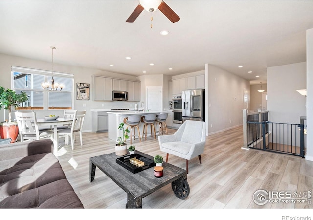 living room featuring light wood-style floors, recessed lighting, baseboards, and ceiling fan with notable chandelier