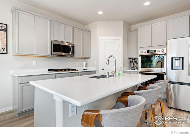 kitchen with stainless steel appliances, a sink, light wood-style flooring, and a kitchen bar