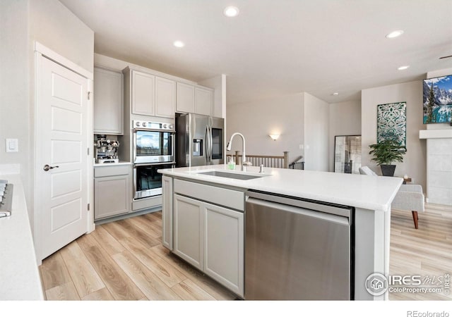 kitchen with light wood-style floors, gray cabinets, stainless steel appliances, and a sink