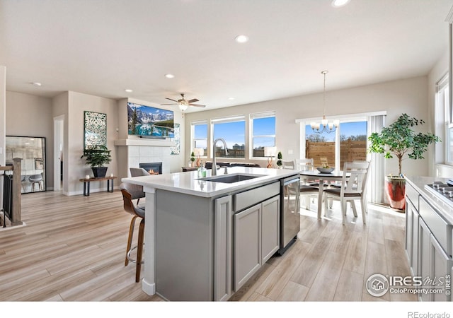 kitchen featuring a tile fireplace, light wood-style flooring, a sink, light countertops, and dishwasher