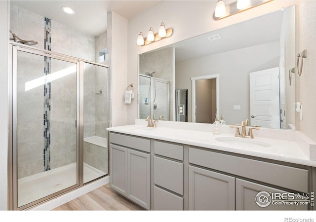 full bathroom featuring double vanity, wood finished floors, a sink, and a shower stall