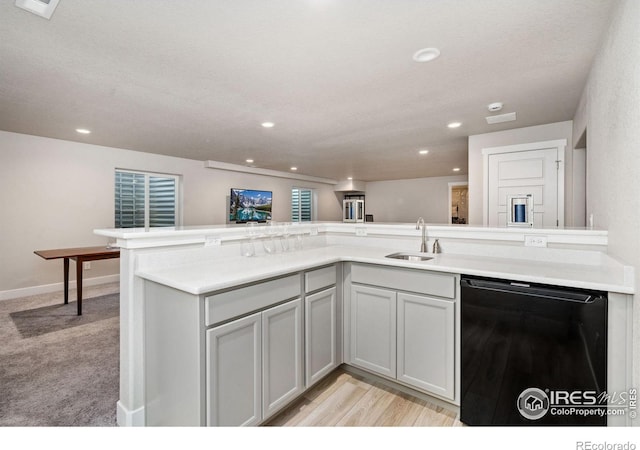 kitchen featuring black dishwasher, light countertops, a sink, and recessed lighting