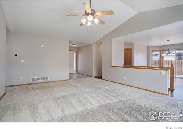 unfurnished living room with lofted ceiling, ceiling fan with notable chandelier, visible vents, baseboards, and carpet