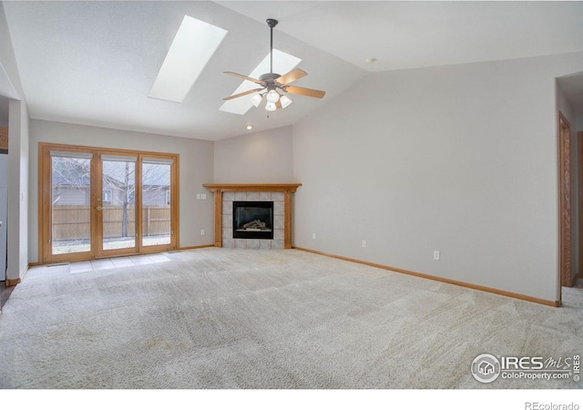 unfurnished living room with carpet, a tiled fireplace, a ceiling fan, vaulted ceiling with skylight, and baseboards