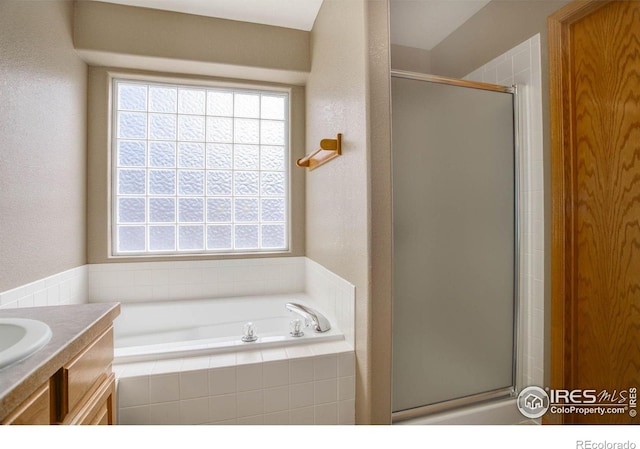 full bathroom with a textured wall, vanity, a shower stall, and a bath