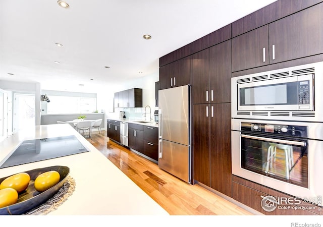 kitchen featuring dark brown cabinets, light countertops, appliances with stainless steel finishes, light wood-style floors, and a sink