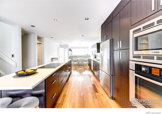 kitchen with a breakfast bar area, light wood-style flooring, stainless steel appliances, light countertops, and modern cabinets