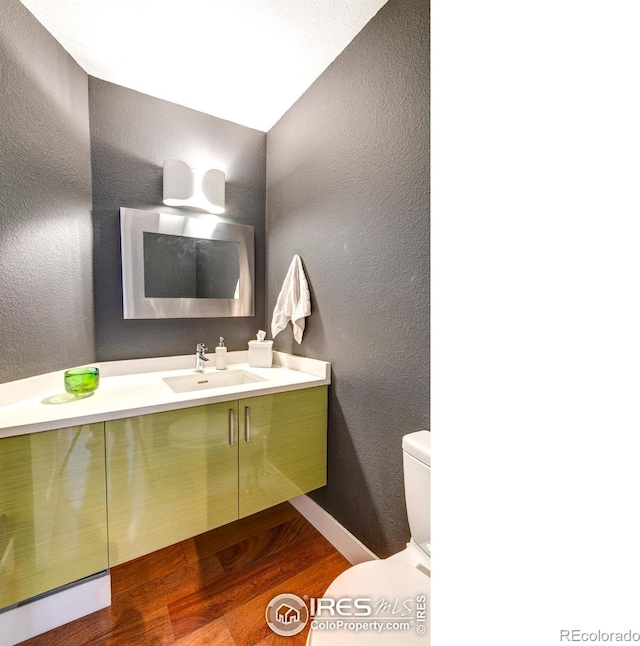 bathroom with wood finished floors, toilet, vanity, and a textured wall