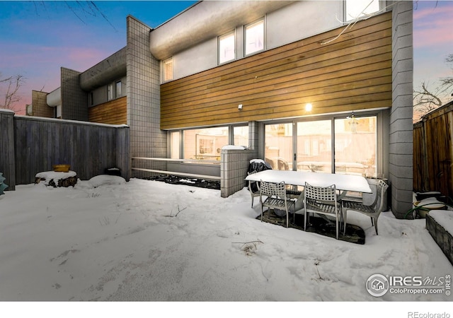 snow covered patio with outdoor dining space and fence