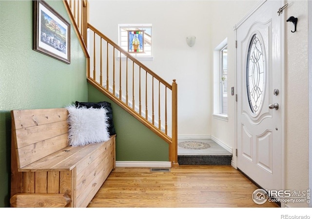 foyer entrance with visible vents, baseboards, wood finished floors, and stairs