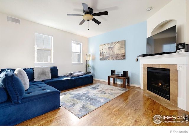 living room featuring wood finished floors, ceiling fan, a tiled fireplace, and visible vents