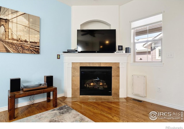 living area with a tile fireplace, visible vents, baseboards, and wood finished floors