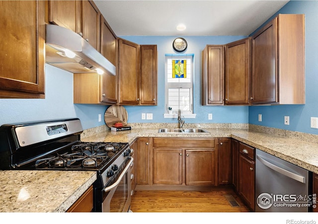 kitchen with a sink, light wood-style flooring, appliances with stainless steel finishes, light countertops, and under cabinet range hood