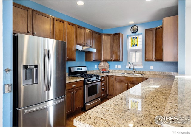 kitchen featuring brown cabinetry, under cabinet range hood, a sink, and stainless steel appliances