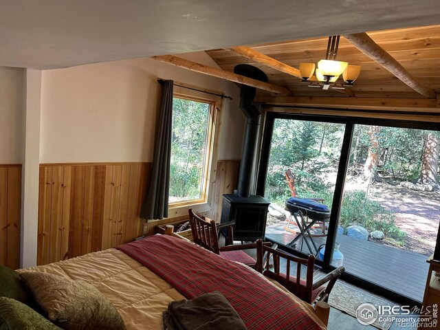 bedroom featuring wooden walls, a wainscoted wall, a wood stove, access to outside, and vaulted ceiling