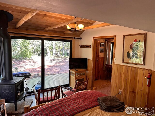 bedroom with a wood stove, a wainscoted wall, vaulted ceiling, and wooden ceiling