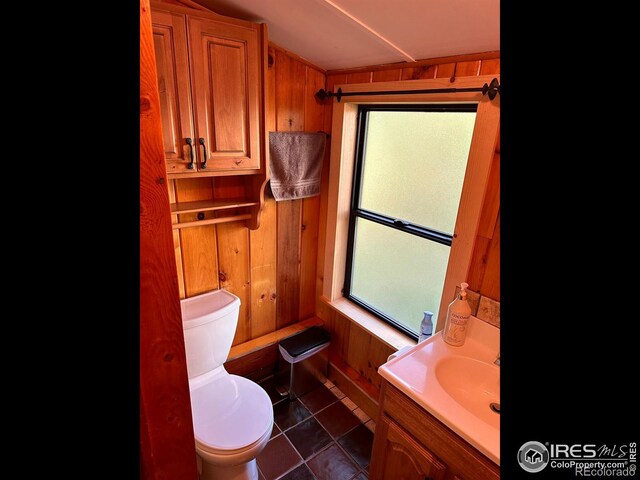 bathroom with toilet, wood walls, tile patterned floors, and vanity