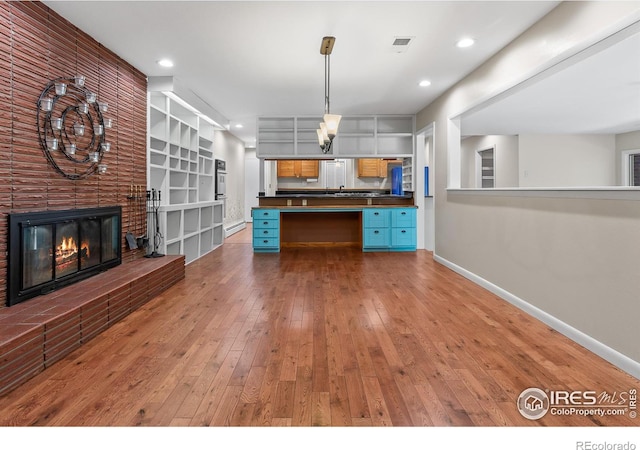 kitchen featuring dark countertops, visible vents, hardwood / wood-style floors, a brick fireplace, and baseboards