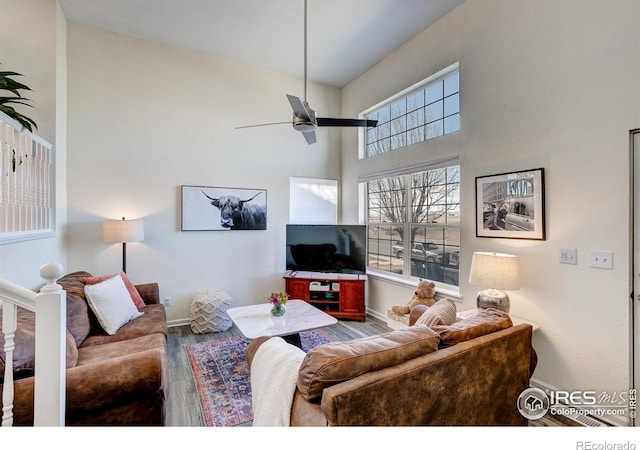 living room featuring a towering ceiling, a ceiling fan, baseboards, and wood finished floors