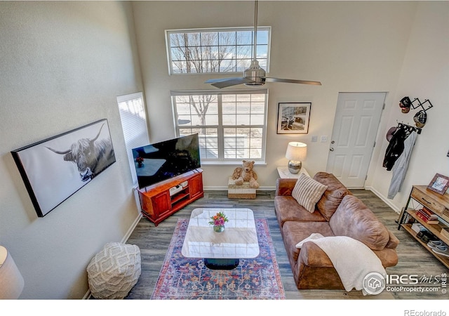 living room featuring baseboards, a high ceiling, a ceiling fan, and wood finished floors