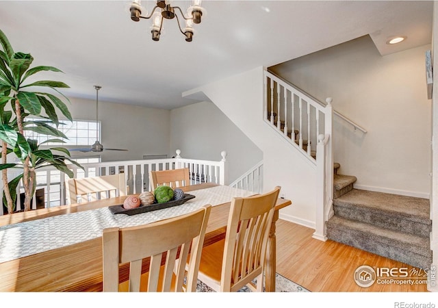 dining space featuring stairs, ceiling fan with notable chandelier, baseboards, and wood finished floors