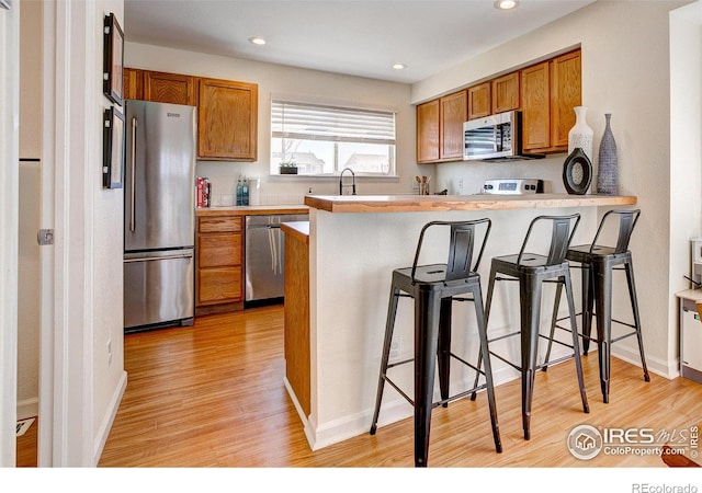 kitchen with brown cabinets, light wood finished floors, a breakfast bar, and stainless steel appliances