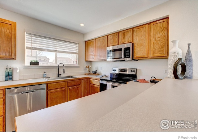 kitchen featuring appliances with stainless steel finishes, brown cabinets, light countertops, a sink, and recessed lighting