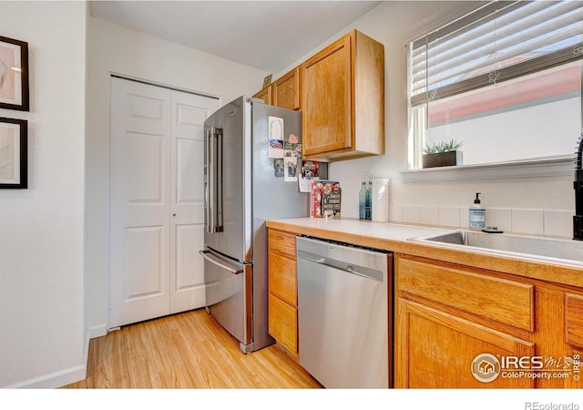 kitchen with appliances with stainless steel finishes, light countertops, a sink, and light wood-style flooring