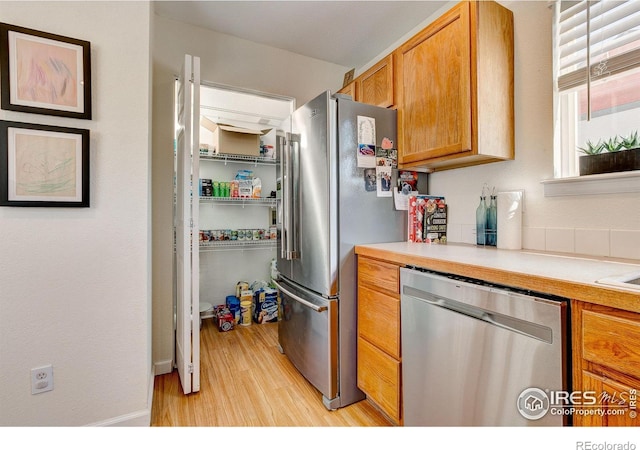 kitchen featuring stainless steel appliances, brown cabinets, light countertops, and light wood-style flooring