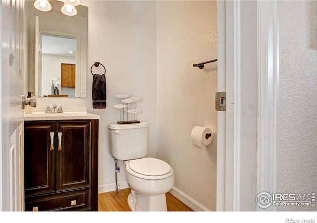 half bath with toilet, baseboards, wood finished floors, and vanity